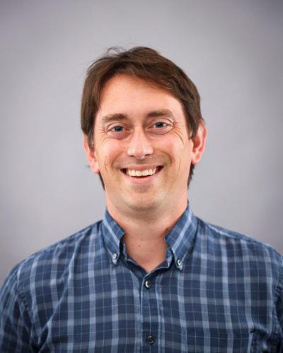 A man wearing a blue plaid shirt smiles for the camera.