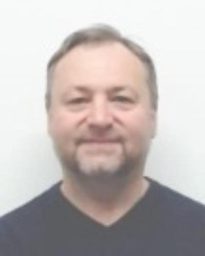 A man with short hair and a beard smiles at the camera against a white background.
