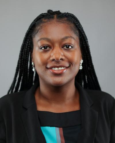 A woman with long dark braids and a warm smile, wearing a black blazer and a colorful top.