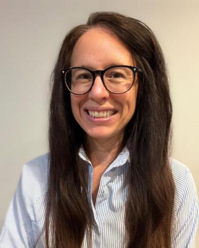 A woman with long dark hair and glasses smiling at the camera.