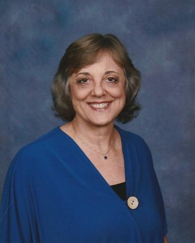 A woman smiles and poses for a portrait, wearing a blue shawl and jewelry.