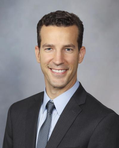 A man in a suit and tie smiles while looking at the camera.