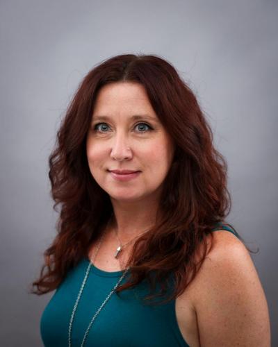 A woman with long red hair and a teal shirt smiles at the camera.