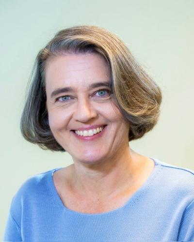 A woman with short hair and a blue shirt smiles while looking at the camera.