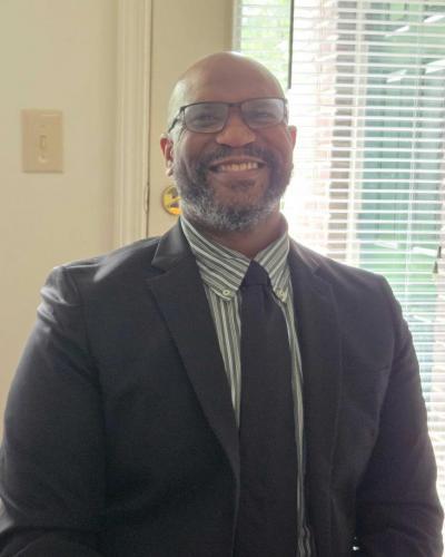 A man in a suit and tie stands in front of a window.