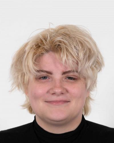 A person with short, blonde hair and a black shirt smiles at the camera.