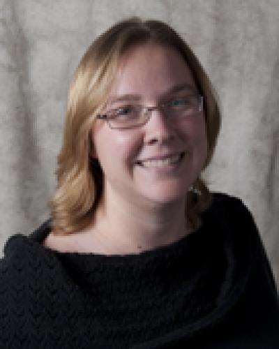 A woman with shoulder-length blonde hair and glasses smiling and wearing a black garment.
