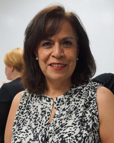 A woman with dark hair and a black and white patterned sleeveless top smiles at the camera.