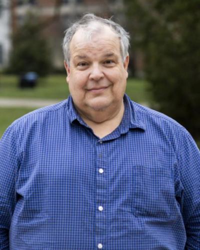 A man stands outside in a blue and white checkered button-up shirt.