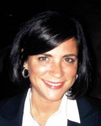 A smiling woman with dark hair and a professional attire consisting of a white collared shirt and a dark blazer.