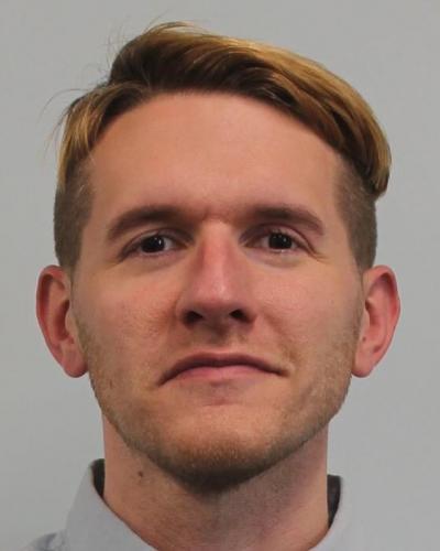 A man with short brown hair looks directly at the camera against a gray background.