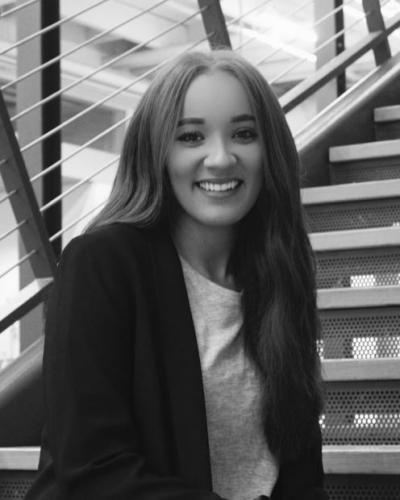 A woman with long hair sitting on a staircase, smiling and looking at the camera.