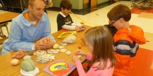 A man sits at a table with several children, all working with clay.