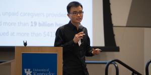 A presenter standing at the podium addressing an audience during a session at the Spring 2026 UK AI/ML Symposium.